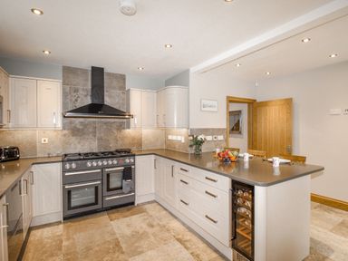 A kitchen with a black stove and range hood white cabinets a countertop with a fruit bowl and two mugs at Family House in Weymouth