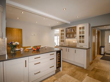 A kitchen with an island counter with fruit bowl and flowers and built in cabinets with glass doors at Family House in Weymouth