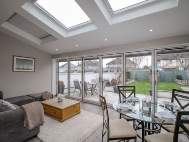 A living room with gray sofa wooden coffee table glass dining table set and large glass doors opening to a garden at Family House in Weymouth