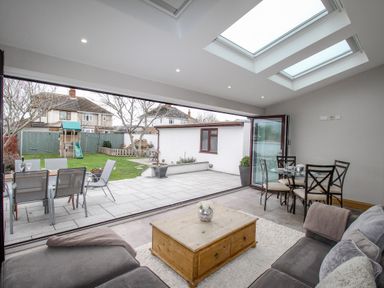 A living room with a wooden coffee table and sofas next to a glass dining table and chairs with skylights and a view of a garden at Family House in Weymouth