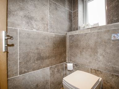 A small bathroom with stone tile walls a toilet a toilet paper holder and a window with decorative items on the ledge at Family House in Weymouth