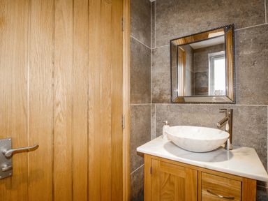 A bathroom with a wooden door a wooden vanity with a marble basin and a mirror on a tiled wall at Family House in Weymouth