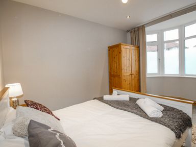 A bedroom with a double bed pillows and rolled towels a wooden wardrobe and a window with curtains at Family House in Weymouth