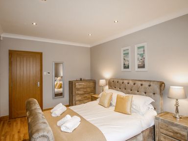 A bedroom with a bed with pillows and towels bedside tables with lamps a dresser a wall mirror and a wooden door at Family House in Weymouth