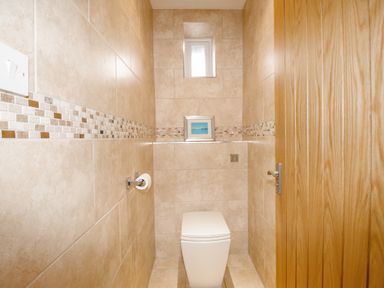 A small bathroom with a toilet a toilet paper holder a wooden door and tiled walls with a small framed picture on the back ledge at Family House in Weymouth