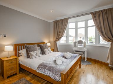 A bedroom with a wooden bed desk lamps and a vanity table by the windows at Family House in Weymouth