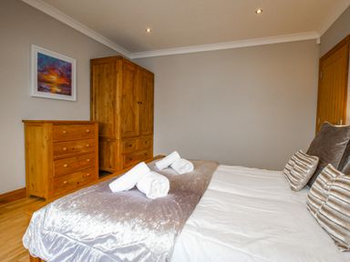 A bedroom with a bed with pillows and rolled towels wooden dresser and wardrobe and a painting on the wall at Family House in Weymouth