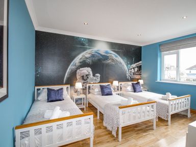 A bedroom with three single beds white bedside tables lamps and a space-themed wall mural at Family House in Weymouth