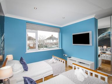 A bedroom with two single beds blue walls and a wall mounted television at Family House in Weymouth