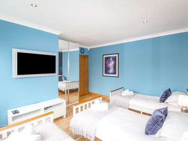 A bedroom with three beds blue walls a wall mounted TV a wooden door and a framed picture at Family House in Weymouth
