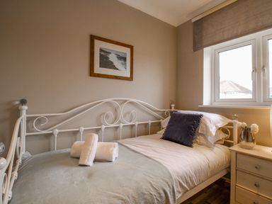A bedroom with a white metal bed frame a pillow rolled towels a nightstand with a vase and flowers and a window at Family House in Weymouth