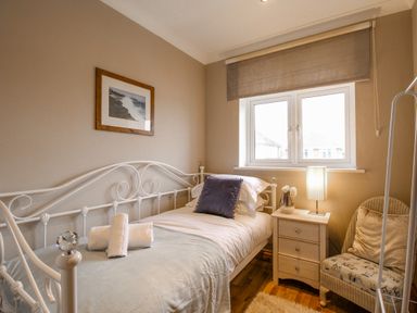 A single bed with folded towels on it a bedside table with a lamp and flowers a window with a blind and a chair with cushions in a bedroom at Family House in Weymouth