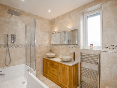 A bathroom with a bathtub shower combination double sink wooden vanity and a window at Family House in Weymouth