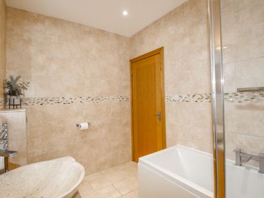 A bathroom with a bathtub sink wooden door and beige tiled walls at Family House in Weymouth