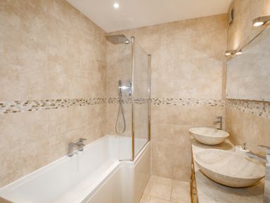 A bathroom with a bathtub a glass shower screen two stone vessel sinks and a large mirror at Family House in Weymouth