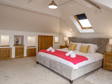 A bedroom with a large bed with white sheets and gold pillows beside wooden nightstands under a skylight at Family House in Weymouth