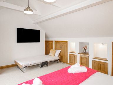 A bedroom with a single bed, a large wall-mounted television, small wooden storage doors, and a bed with a pink cover and rolled towels at Family House in Weymouth