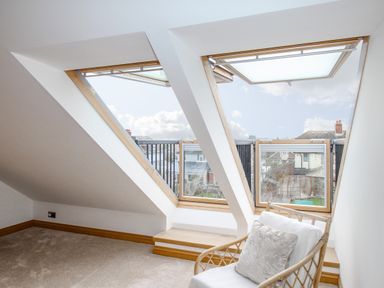 A room with slanted ceilings two large open skylight windows and a chair with a cushion at Family House in Weymouth