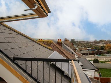 View of rooftops with solar panels and chimneys from an open skylight window at Family House in Weymouth