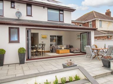 A patio area with outdoor dining furniture and planters outside a house with an open living room and dining area at Family House in Weymouth