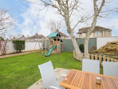 A garden with a wooden playset and slide a patio table with chairs and a tree at Family House in Weymouth