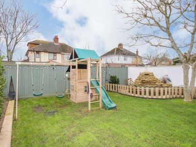 A backyard with a children's playset including swings and a slide and a small rock fountain surrounded by a wooden fence at Family House in Weymouth