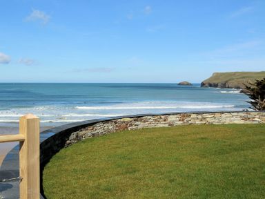 A curved stone wall overlooking a grassy area and the ocean with waves and distant cliffs at The White House in Polzeath