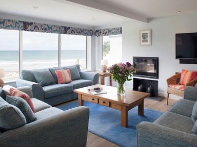 A living room with blue sofas a wooden coffee table with flowers and a fireplace at The White House in Polzeath
