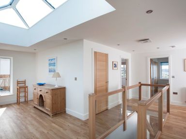 A hallway with wooden floors a wooden cabinet a chair and a skylight at The White House in Polzeath
