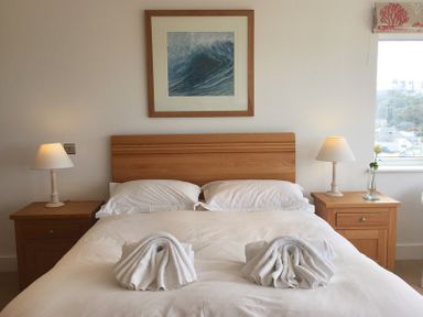 A bedroom with a made bed and folded towels on it two bedside tables with lamps a framed wave picture above the bed at The White House in Polzeath