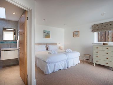 A bedroom with two beds and a chest of drawers next to a bathroom at The White House in Polzeath