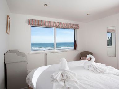 A bedroom with a bed featuring towel swans a window with an ocean view a chair and a mirror at The White House in Polzeath