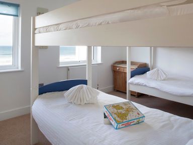 A bedroom with bunk beds a wooden desk and two windows with sea views at The White House in Polzeath