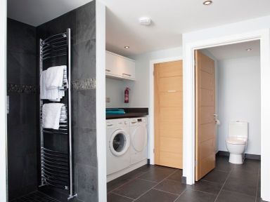 A laundry area with a washing machine and dryer a towel rail with towels and an adjacent toilet at The White House in Polzeath