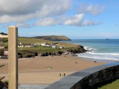 A sandy beach with people, coastal cliffs, houses, grass fields, and a blue sea at The White House in Polzeath