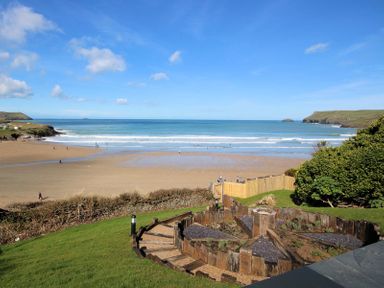 A sandy beach with people near the water and green grassy area with wooden garden beds at The White House in Polzeath