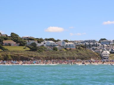 A beach with many people near the shore and houses on a hill overlooking the beach at The White House in Polzeath