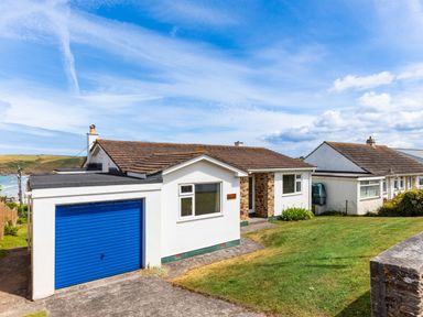 A white house with a blue garage door and a lawn at Zapadiah in Polzeath
