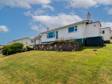 A white single story house with large windows and a garden on a grassy hill at Zapadiah in Polzeath