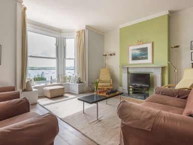 A living room with armchairs a coffee table a fireplace a television and a bay window overlooking water at 4 The Terrace Rock
