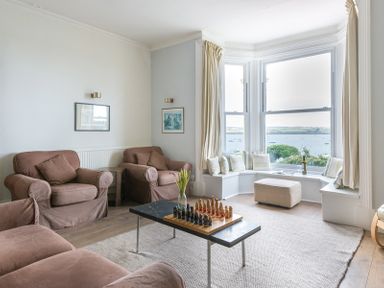 A living room with brown armchairs a bay window with seating and a chess board on a coffee table at 4 The Terrace in Rock