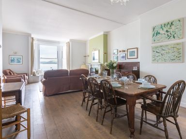 A dining room with a wooden table set for six chairs and a sitting area with couches and armchairs by a window at 4 The Terrace in Rock