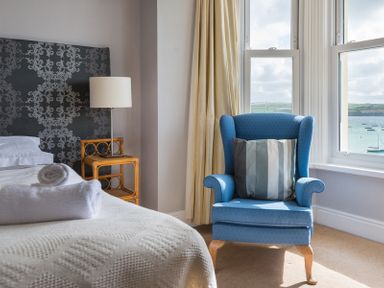 A bedroom with a bed with folded towels a side table with a lamp and a blue armchair with a pillow by a window at 4 The Terrace in Rock