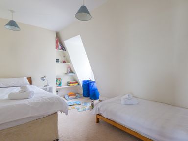 A bedroom with two single beds a bedside table and shelves with toys and books at 4 The Terrace Rock