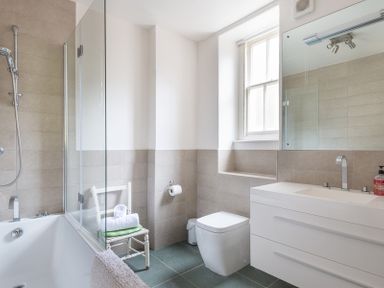 A bathroom with a bathtub shower combination a white chair with towels a toilet and a sink with a mirror at 4 The Terrace in Rock