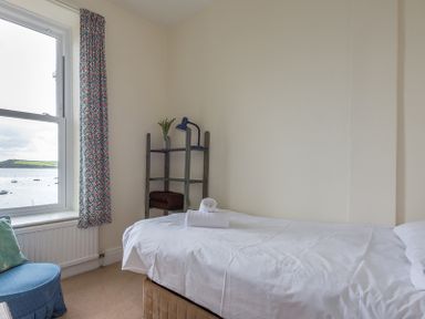 A bedroom with a single bed a small shelving unit and a window overlooking water at 4 The Terrace in Rock