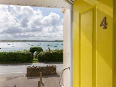 View through an open yellow door with number 4 onto a road hedge and water with boats at 4 The Terrace Rock