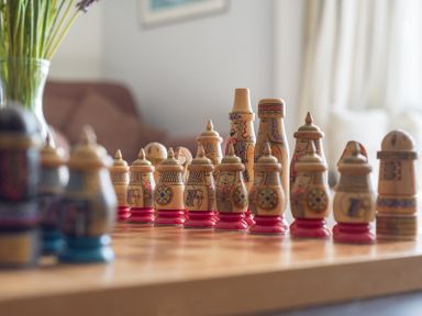 A close-up of carved wooden chess pieces on a chessboard with a vase of flowers and a sofa in the background at 4 The Terrace in Rock