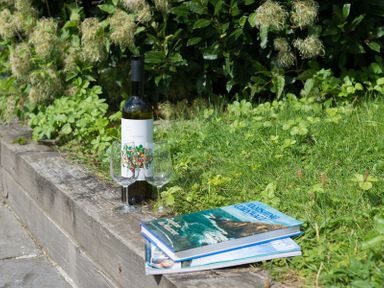 A wine bottle with two glasses and two books on a wooden ledge next to grass and plants at 4 The Terrace in Rock