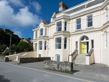 A street view of a large cream colored house with a yellow door and bay windows at 4 The Terrace in Rock